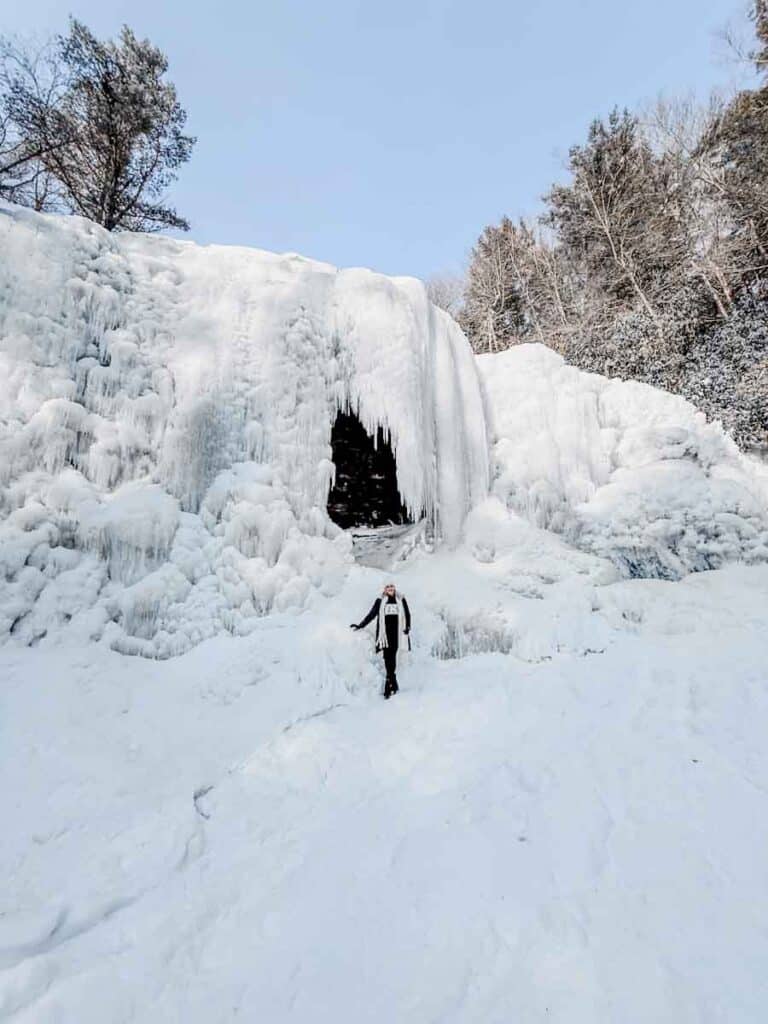 A woman stands before a frozen waterfall at Swallow Falls State Park, a stunning winter spot near Deep Creek Lake, Maryland.