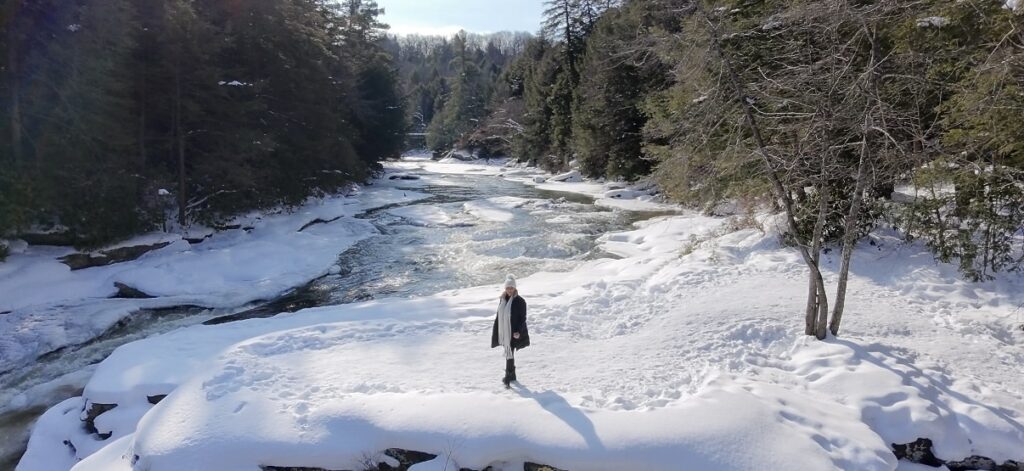 Drone view of Swallow Falls State Park in winter near Deep Creek Lake, MD, with a snowy river, frozen waterfalls, and pines.